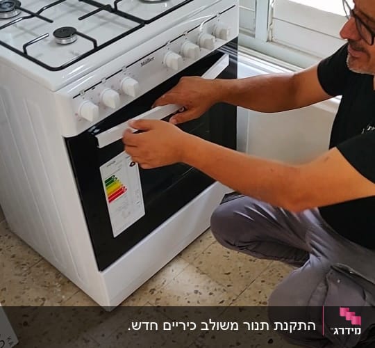אדם מתקין מדבקה על תנור גז לבן במטבח.